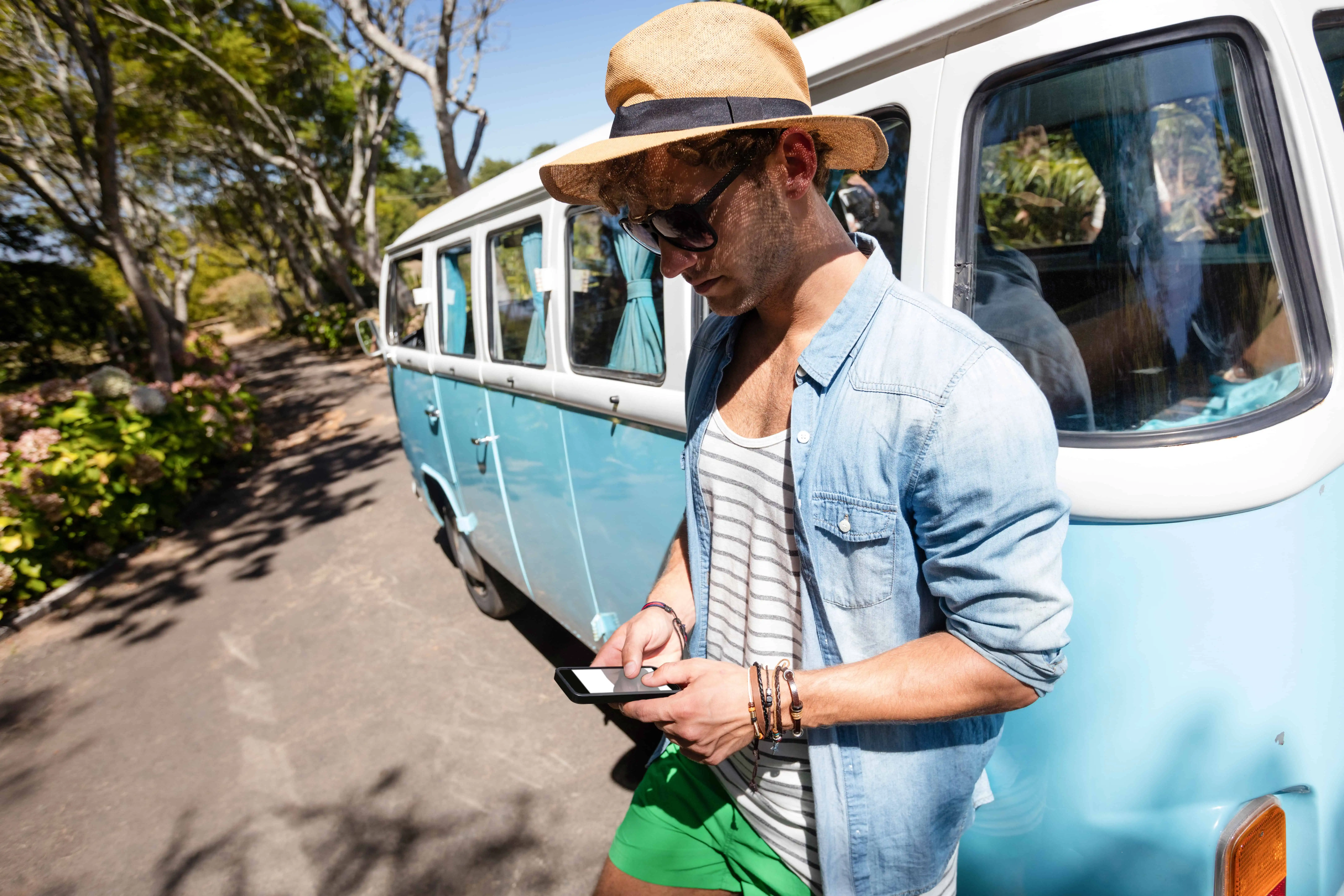 Man standing near campervan and using mobile phone in park