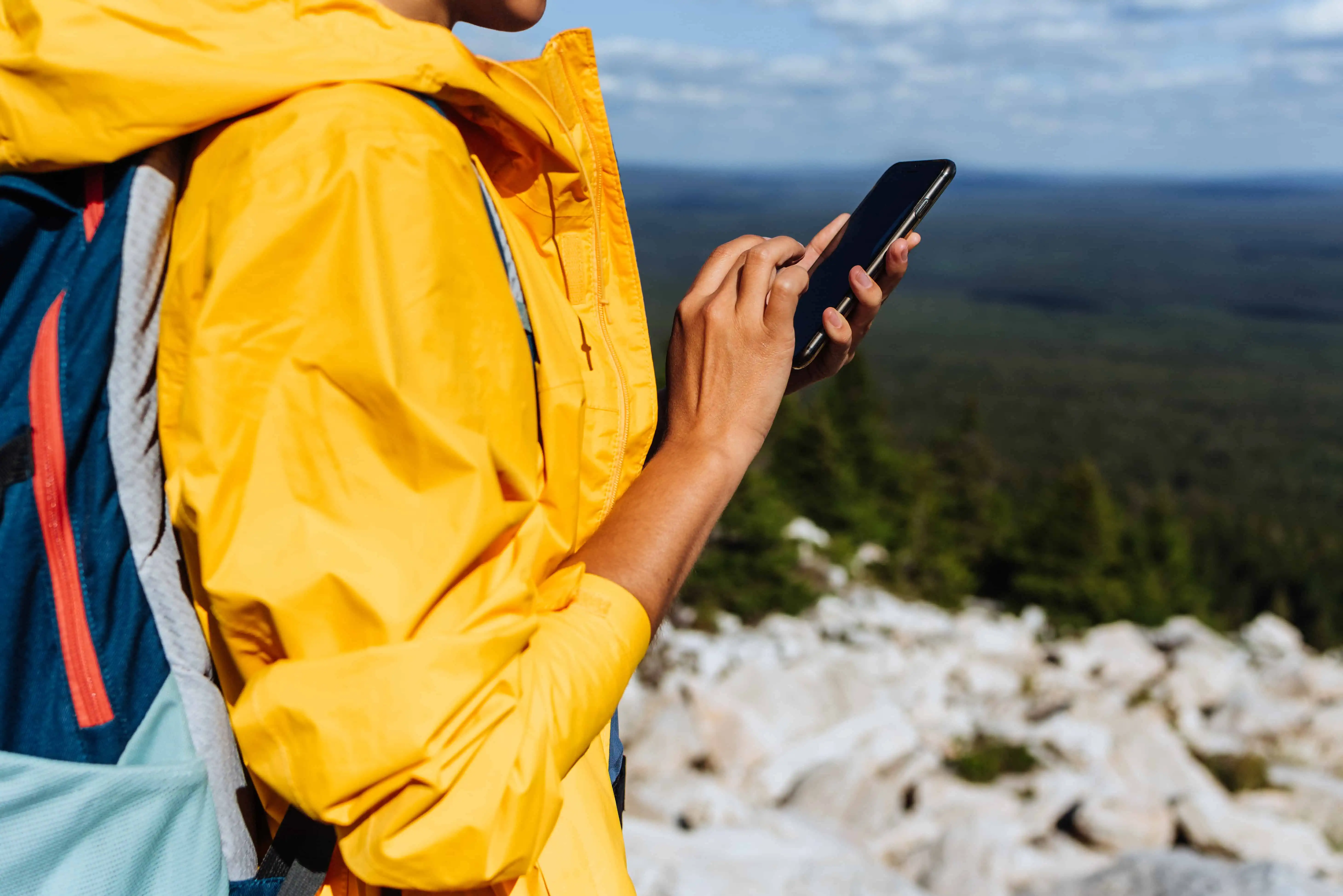 A traveler with a phone, close-up.Young woman wearing yellow windbreaker use smartphone search map at countryside background. Adult woman holding and using smartphone. Travel and active lifestyle