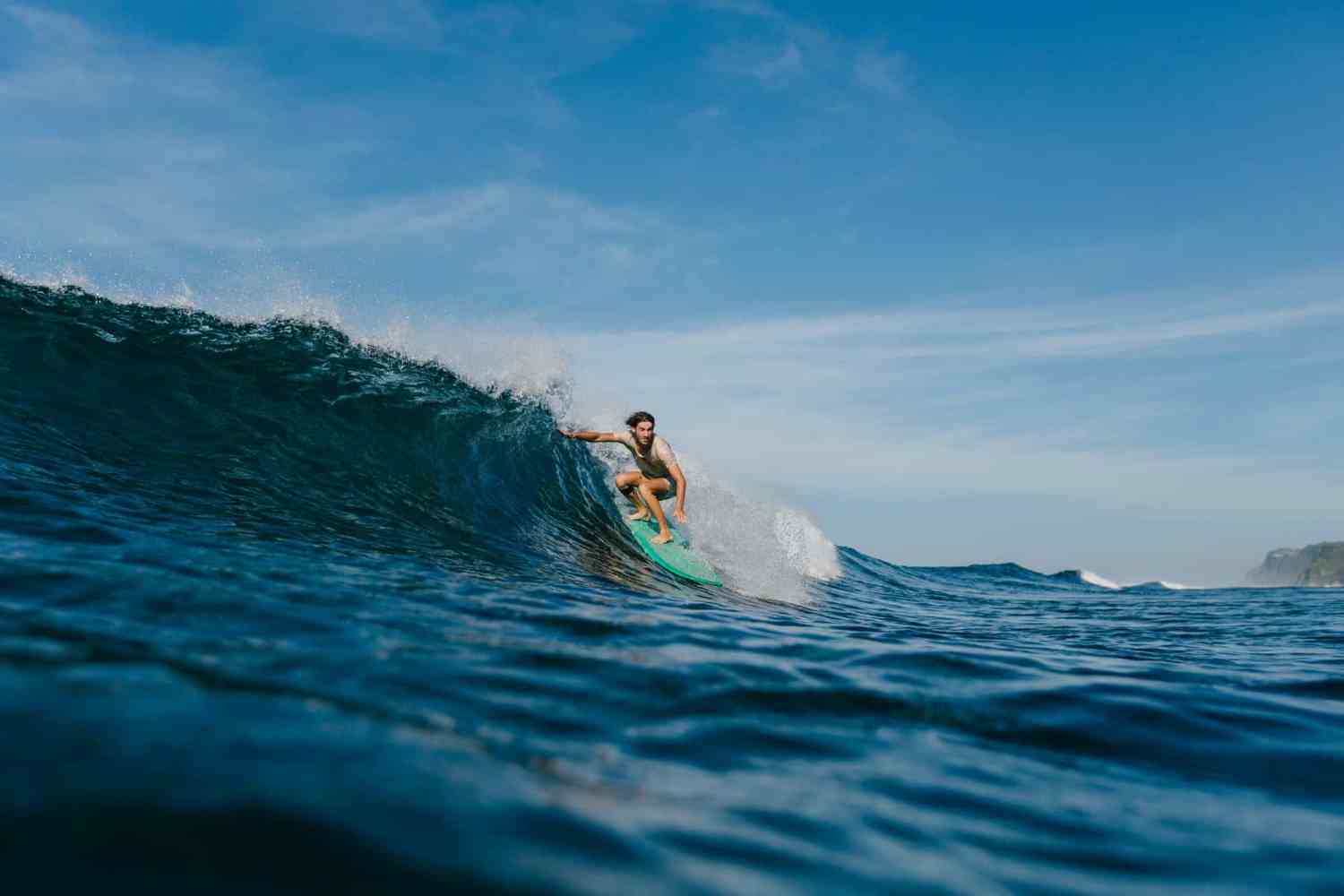 professional surfer in wet t-shirt riding waves on surfboard on sunny day