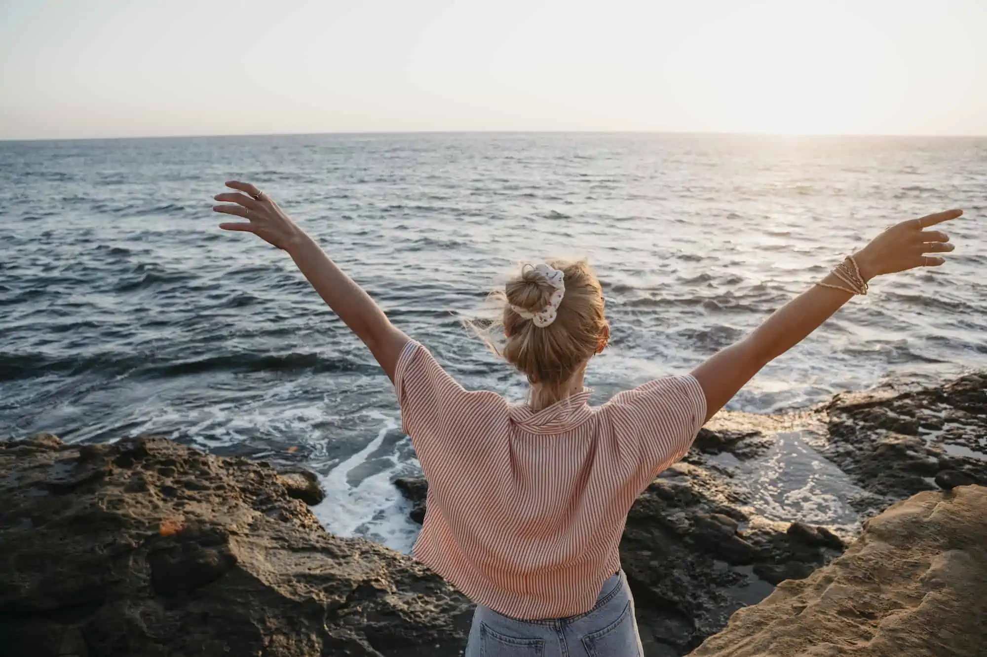 Rear view of young woman at the sea with raised arms, Sunset Cliffs, San Diego, California, USA