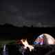 Tourists near campfire and tent under night starry sky