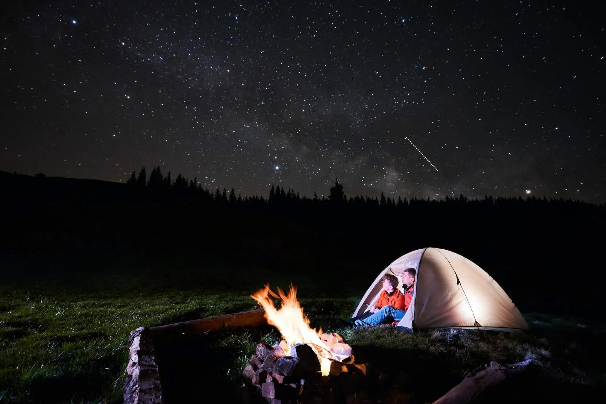Tourists near campfire and tent under night starry sky