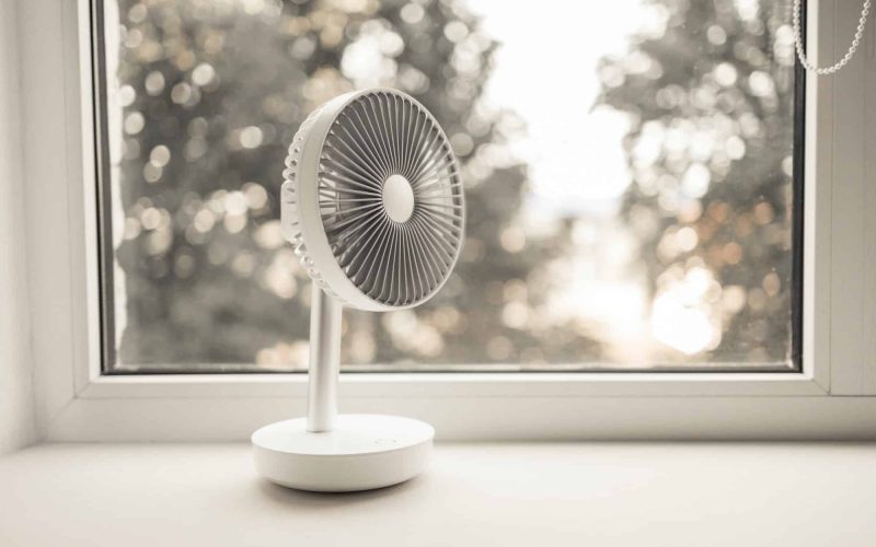 Modern electric portable fan in bedroom. Cooling of high air temperature. Minimal style, copy space.