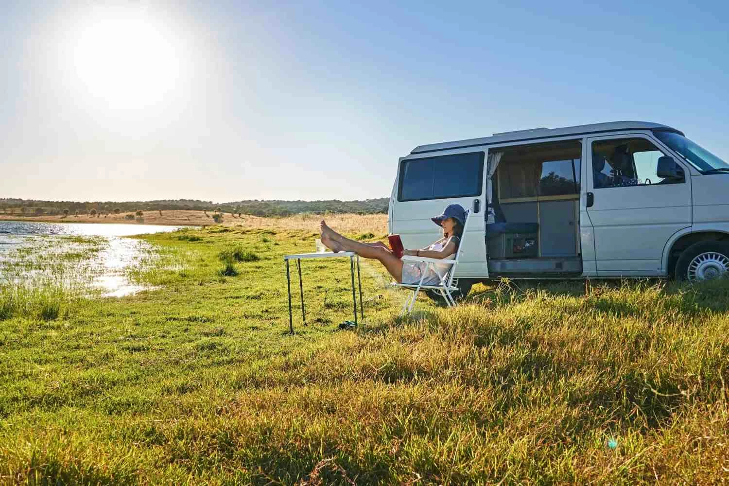 Lady sitting on chair near table and reading book on shore of river