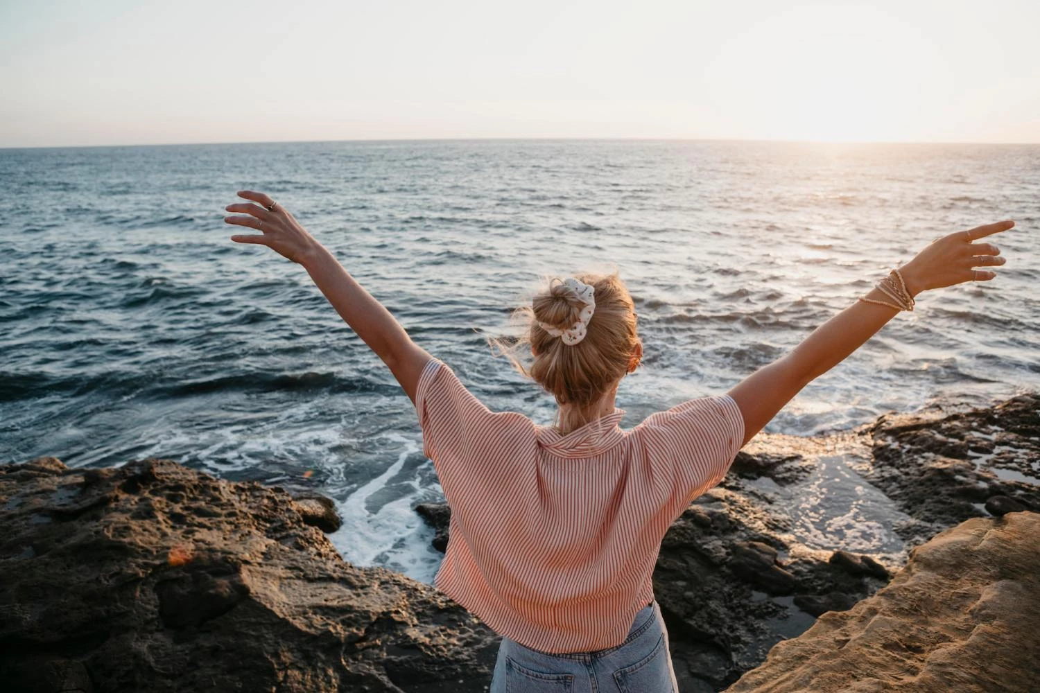 Rear view of young woman at the sea with raised arms, Sunset Cliffs, San Diego, California, USA